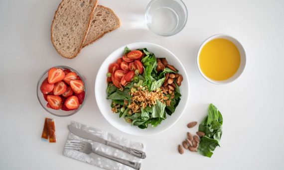 Top view of a healthy salad and fresh ingredients with bread and juice on a white surface.
